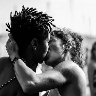 Two people kissing, one holding the other other's head, in the middle of a queer pride parade in Marseille, France