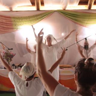 Several Kundalini practitioners, dressed in white, lift their arms as they chant