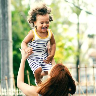 A toddler laughs, mid air, as an adult lifts the toddler into the air.
