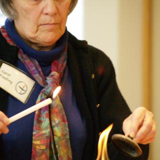 Holding a small lit candle, a UU named Carol lights a large chalice flame