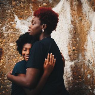 A black parent embraces their child, who is smiling in to the camera