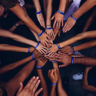 A circle of people, from above, with hands extended into the center of a circle.
