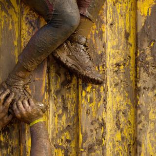 A pair of muddy arms reaches up to push a muddy foot, as if helping someone climb a wall.