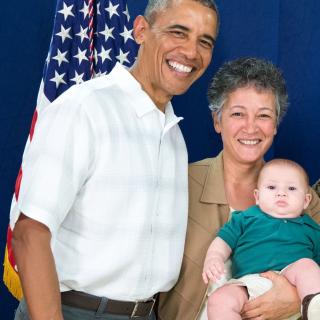 Photo of Rev. Nayer Taheri holding a baby and standing next to President Barack Obama and an American flag.