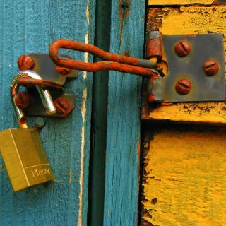 open padlock and rusty clasp on green blue and yellow flaking painted wooden garden shed