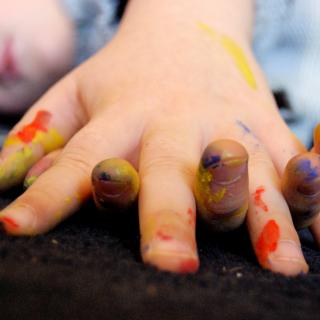 a small child's hands, clasped, with patches of red, yellow, and blue paint