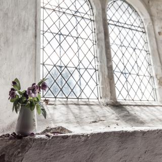 A pitcher of flowers rests on the windowsill inside a room reseembling a chapel