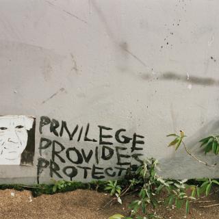 At the bottom of a wall, three words are painted: privilege provides (+) protects
