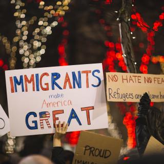A sea of signs, at a protest, above people's heads: "Immigrants make America great" and "No hate no fear."