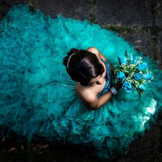 A Latina girl in a full, formal teal gown, and holding a bouquet of turquoise flowers, shot from above.