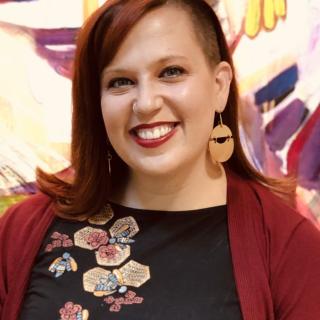 Rev. Ashley Horan smiles, wearing rad earrings and a bold red lip.