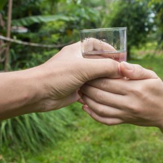 A person, with two hands, receives a glass of water from another person. 
