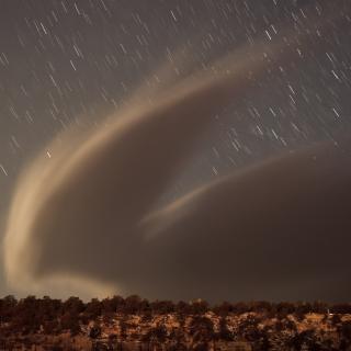 A wind-driven cloud over the south rim of the Grand Canyon, with stars in the background