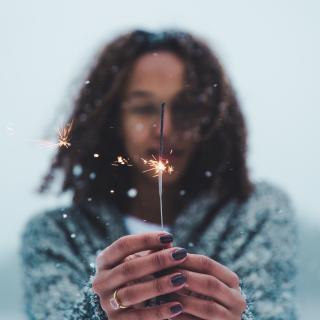 In the snow, with only their upper body visible, a person holds a lit sparkler.