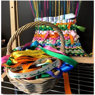 Basket of colorful ribbons with words expressing emotions in front of loom with woven ribbons