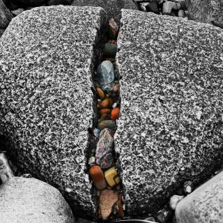 A large gray rock is cracked down the middle, where many small colorful stones are caught