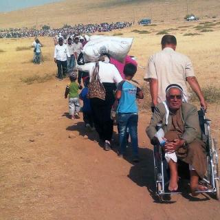 A long line of Syrian Kurdish refugees travel across a parched field intoto Turkey
