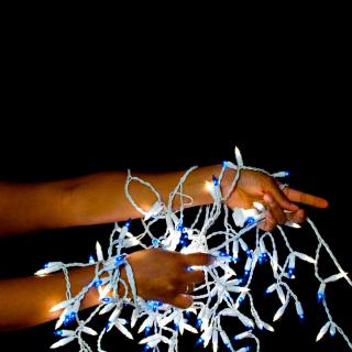 A string of lit Christmas lights, with small white bulbs, tangled around a person's arms.