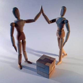 Two wood artists' models high-five over a wood puzzle
