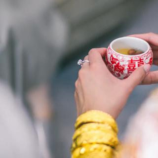 A woman's hands -- on which there is a large wedding ring -- hold a cup, with Chinese characters on the sides, containing tea..