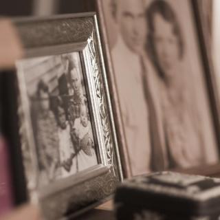 A close-up of framed photographs. In the foreground, a blurry color photo of two people. In the background, vintage-looking black-and-white photos of couples.