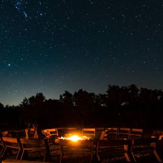 a fire is surrounded by chairs under a starry night sky