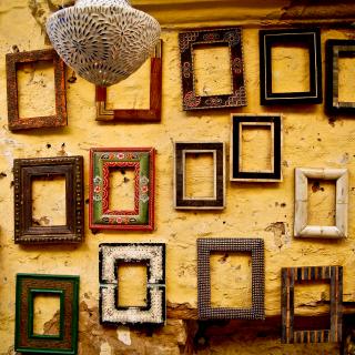 Against a rough plaster wall, about 19 empty picture frames -- each unique -- hang in an informal arrangement