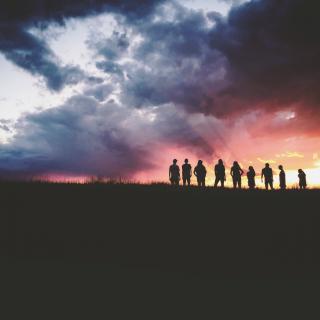 From a distance, a group of people is silhouetted by a vibrant sunset.