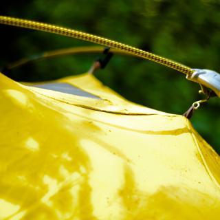 A close-up of the side of a bright yellow tent, with its fabric hung from taught tent poles.