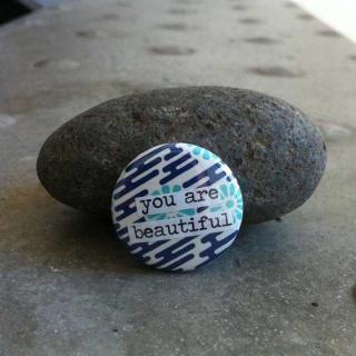 A small button, leaning against a rock, that says "you are beautiful"