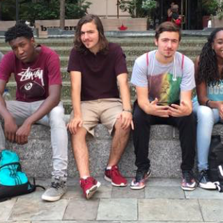 several youth of varying racial identities and genders sit on a bench, some looking serious, some being silly